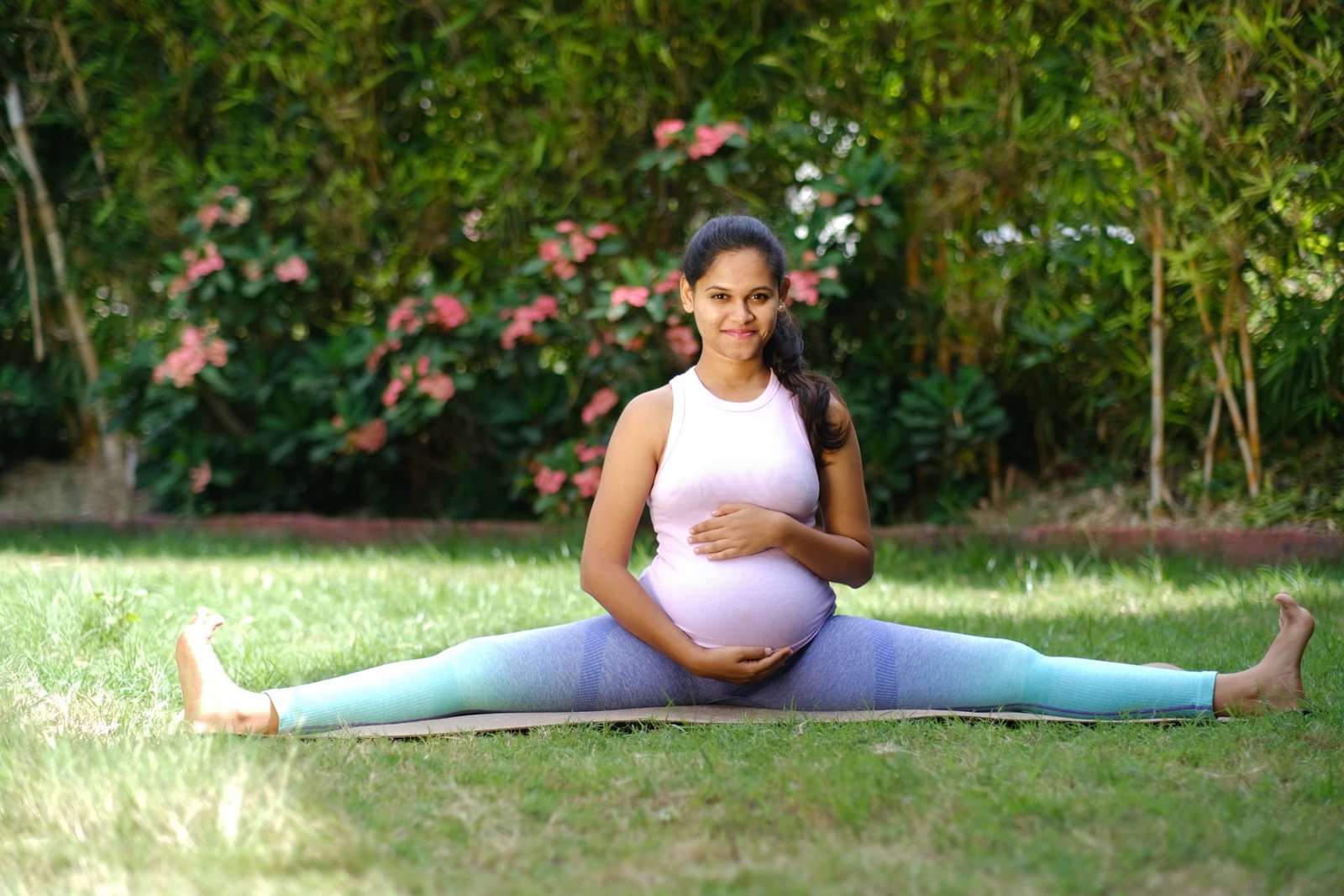 Yamini seated in a wide-legged stretch, hands resting on her belly